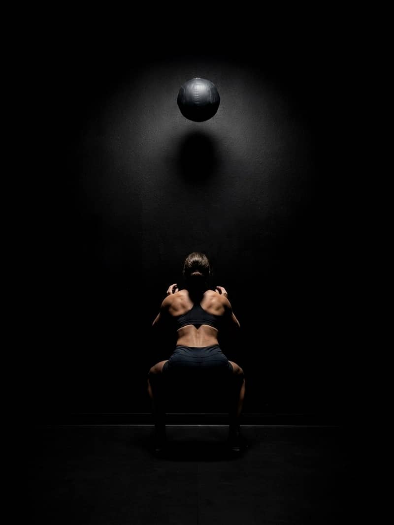 An athlete under a loaded barbell in a rack, lit from above
